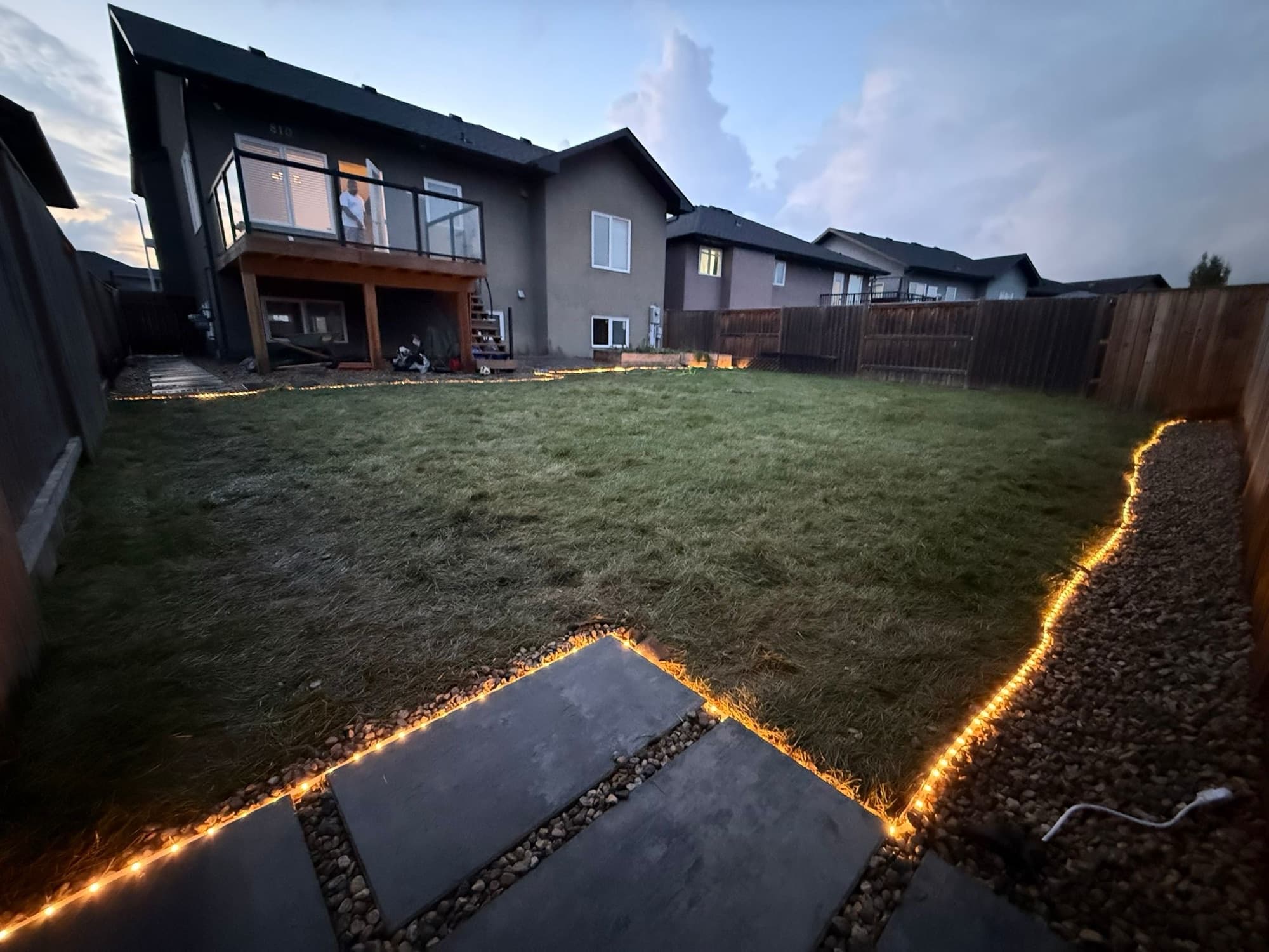 Stoonex Services backyard build at dusk with warm perimeter lighting in Saskatoon
